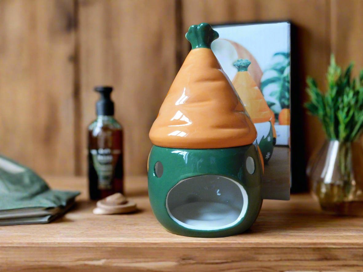 A ceramic oil/wax burner in the shape of a gnome / gonk with a carrot patch on the hat, placed on a wooden shelf. View from the back