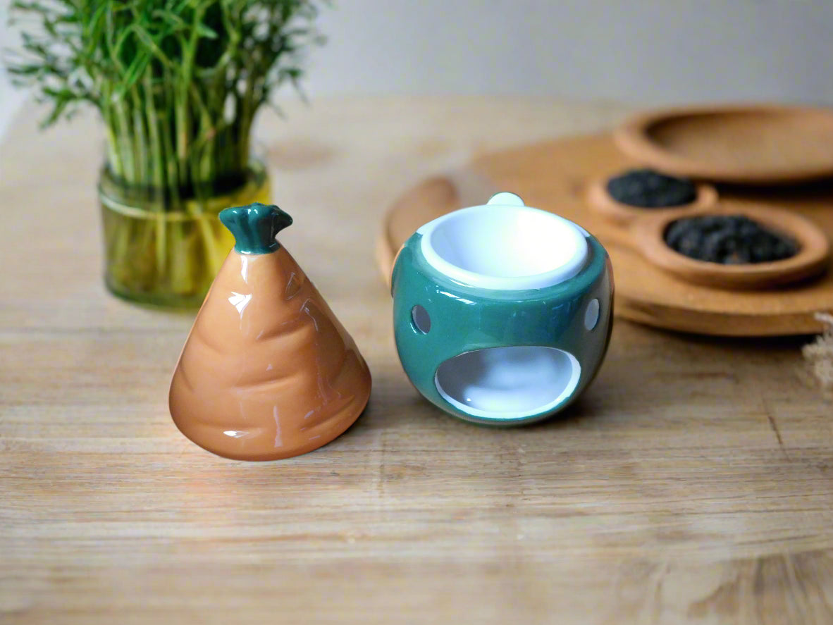A ceramic oil/wax burner in the shape of a gnome / gonk with a carrot patch on the hat, placed on a wooden shelf. View from the back with the hut on the top of the table