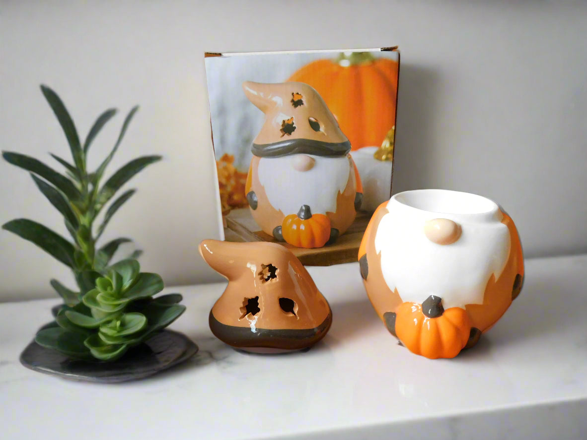 Ceramic oil/wax burner with a design of a Gonk, in orange and brown colors, placed on a white surface with a plant to its left. The hut of the gonk is on the top of the counter