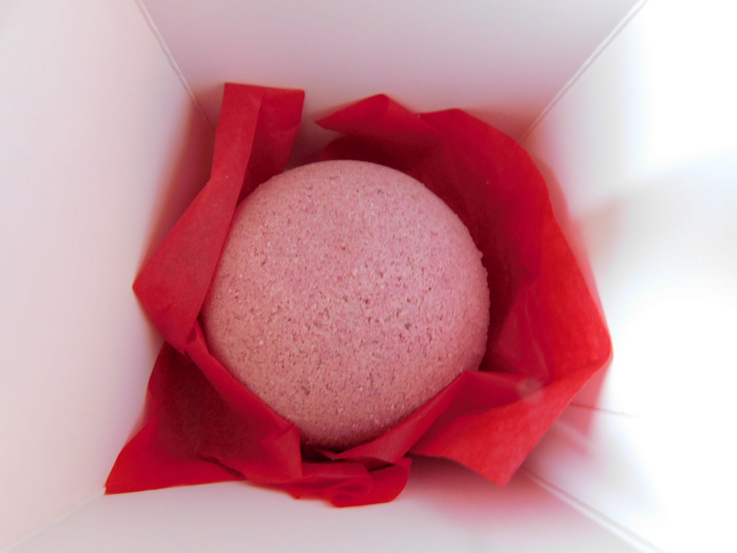 Pink bath bomb wrapped in red paper inside a white box
