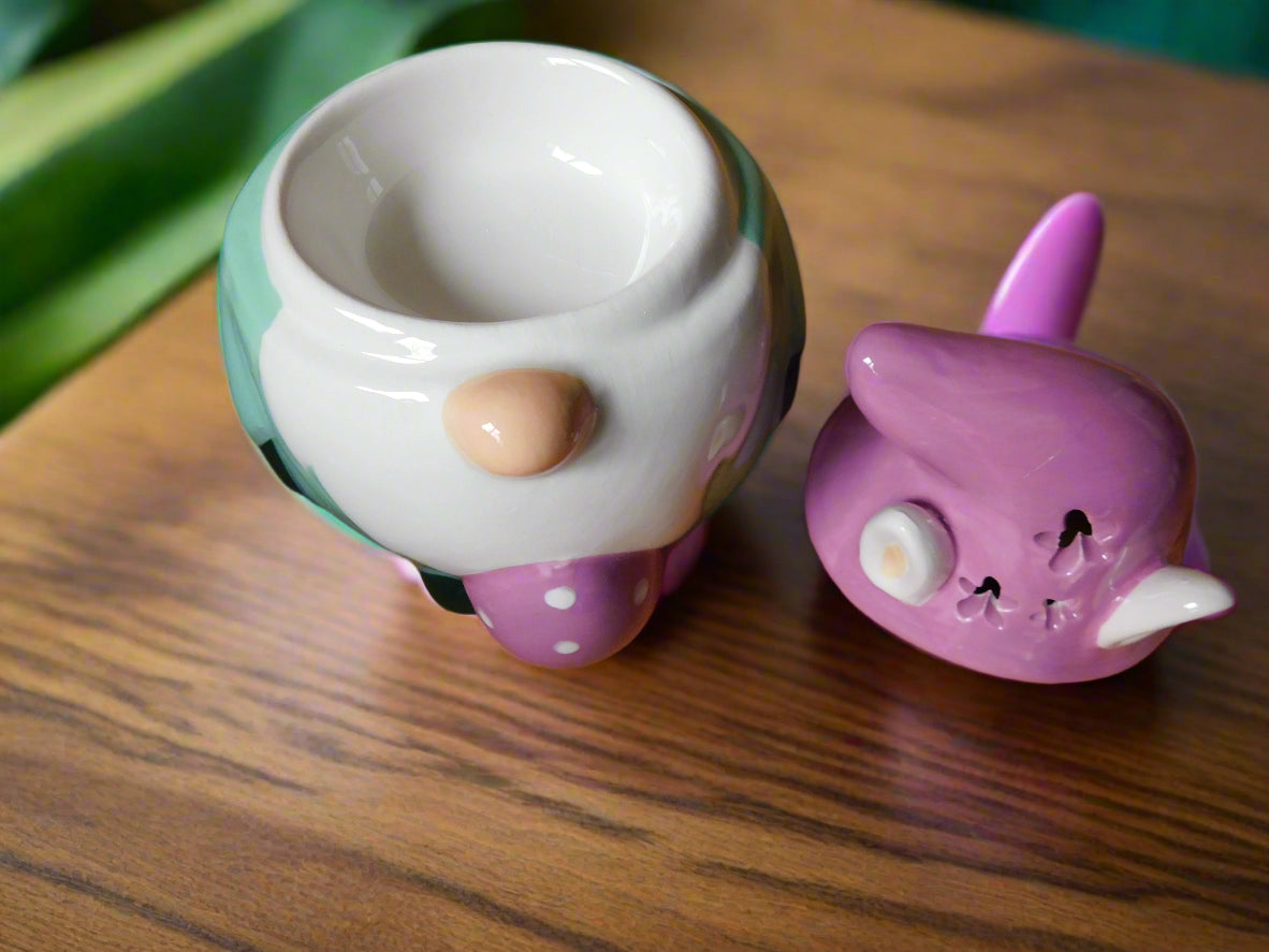 A ceramic oil/wax burner in the shape of a bunny gonk with decorative elements, displayed on a wooden surface view from the top