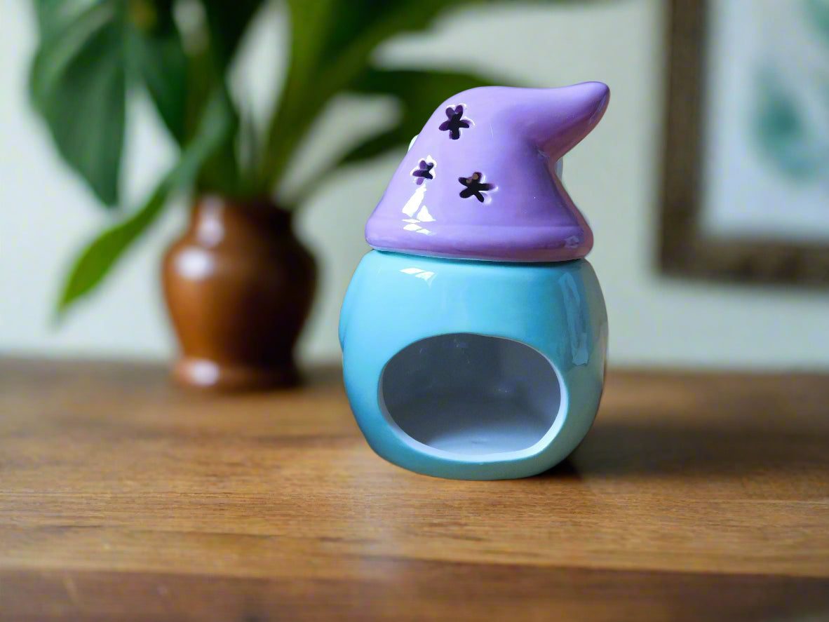 A ceramic oil/wax burner in the shape of a bunny gonk with decorative elements, displayed on a wooden surface with foliage in the background view from the back
