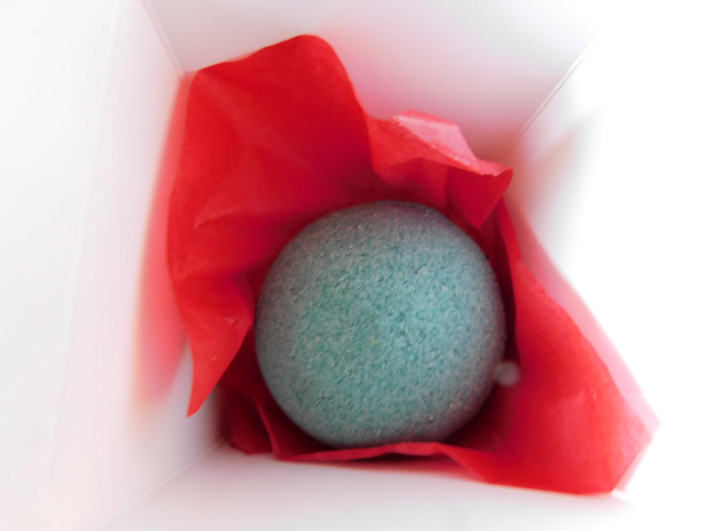 Green bath bomb wrapped in red tissue paper on a white background