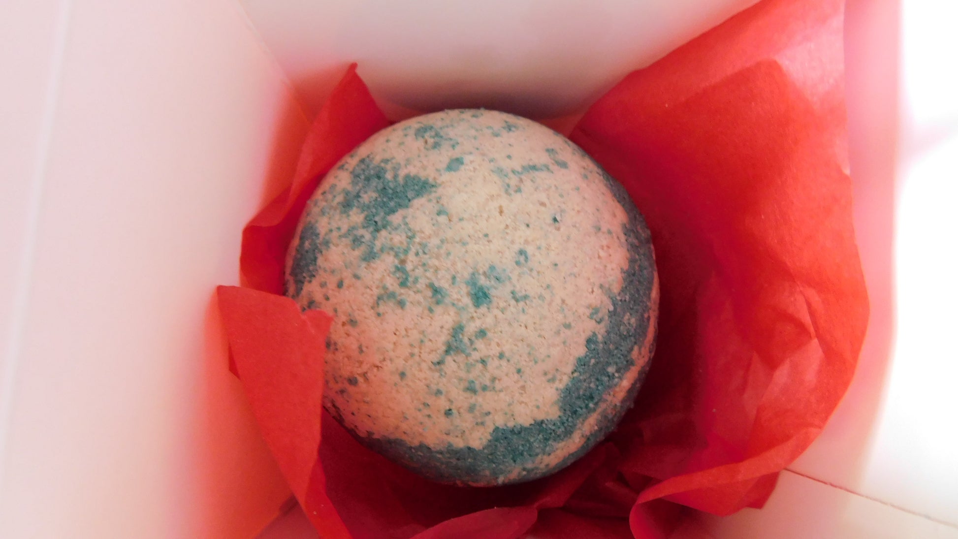 Bath bomb with green speckles in a red box