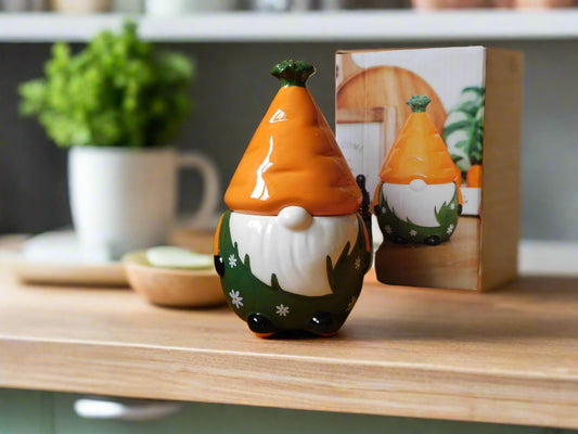 A ceramic oil/wax burner in the shape of a gnome / gonk with a carrot patch on the hat, placed on a wooden shelf.