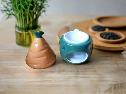 A ceramic oil/wax burner in the shape of a gnome / gonk with a carrot patch on the hat, placed on a wooden shelf. View from the back with the hut on the top of the table