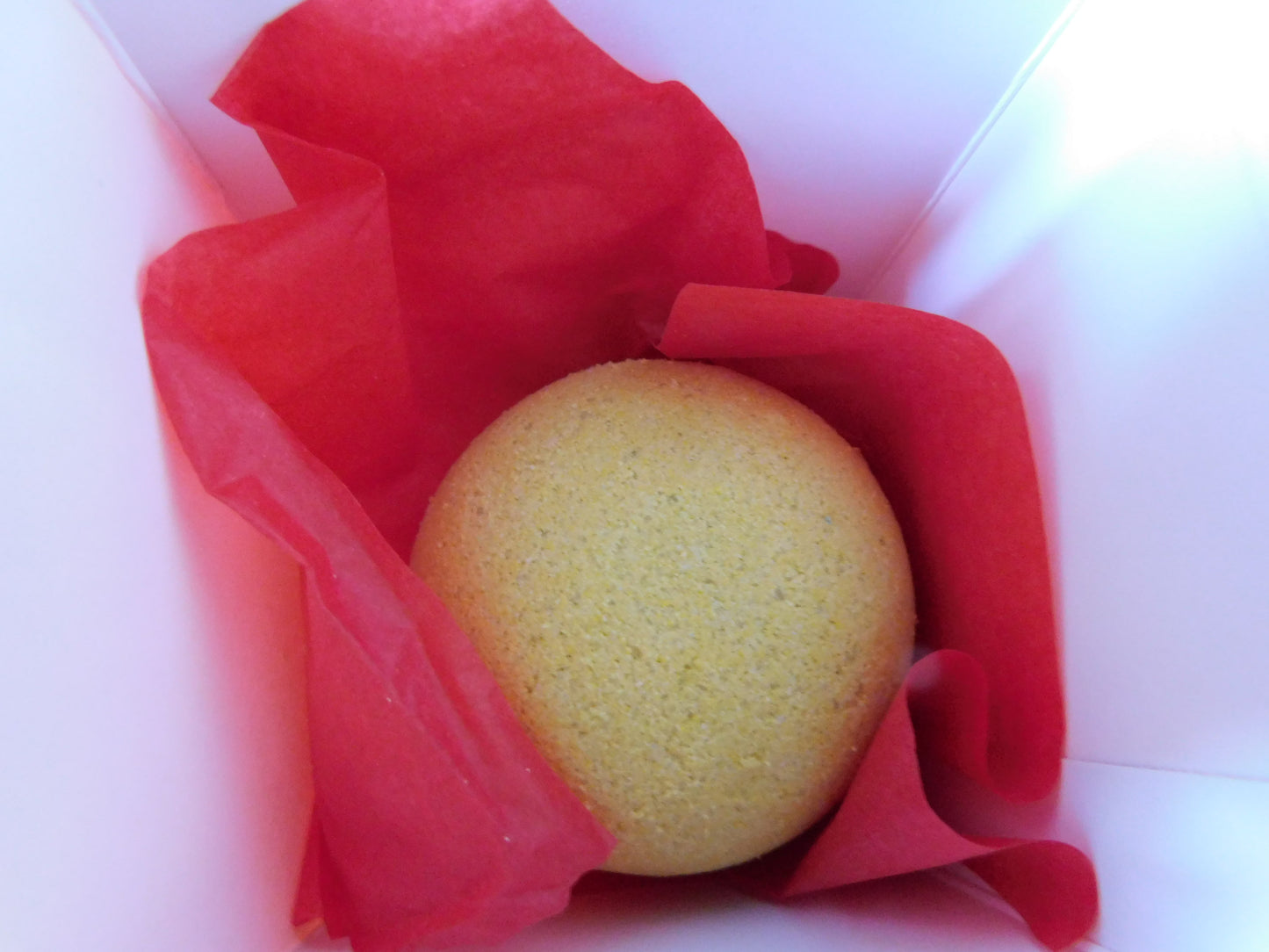 Yellow bath bomb in a red box with red tissue paper on a white background