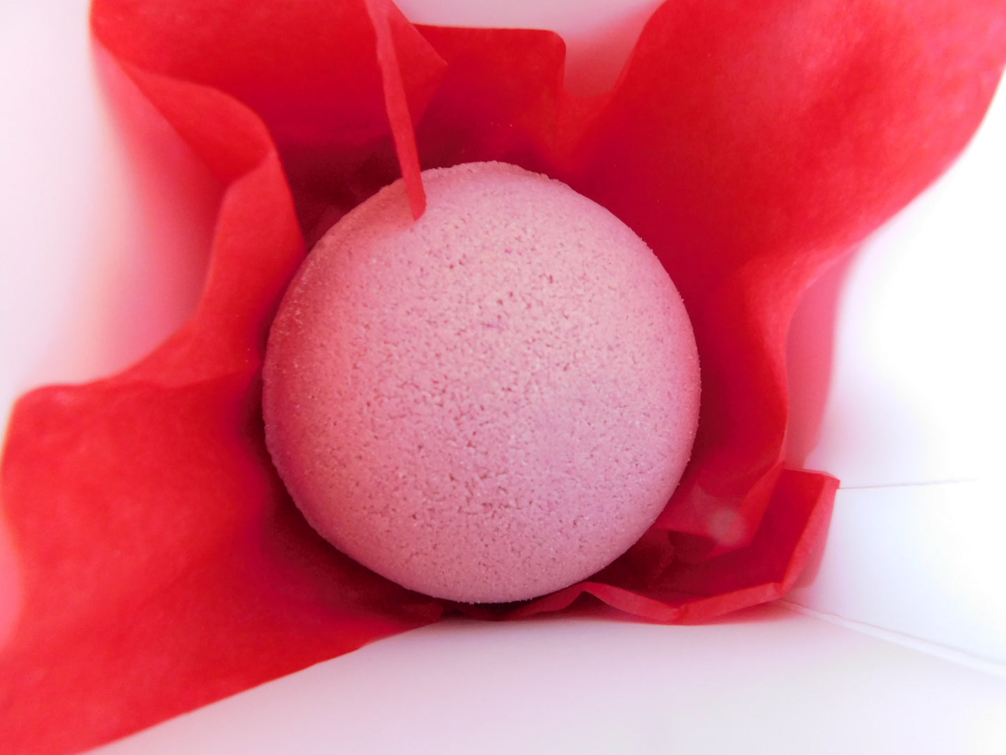 Pink bath bomb in a red tissue on a white background in a red box