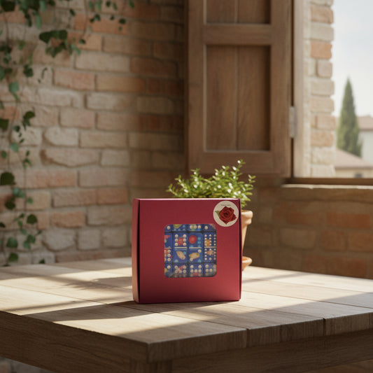 A square magenta-purple cardboard box with a clear plastic window showing a blue domino set inside, photographed on a tan textured surface. A small round sticker with a red rose is visible in the top right corner of the box.