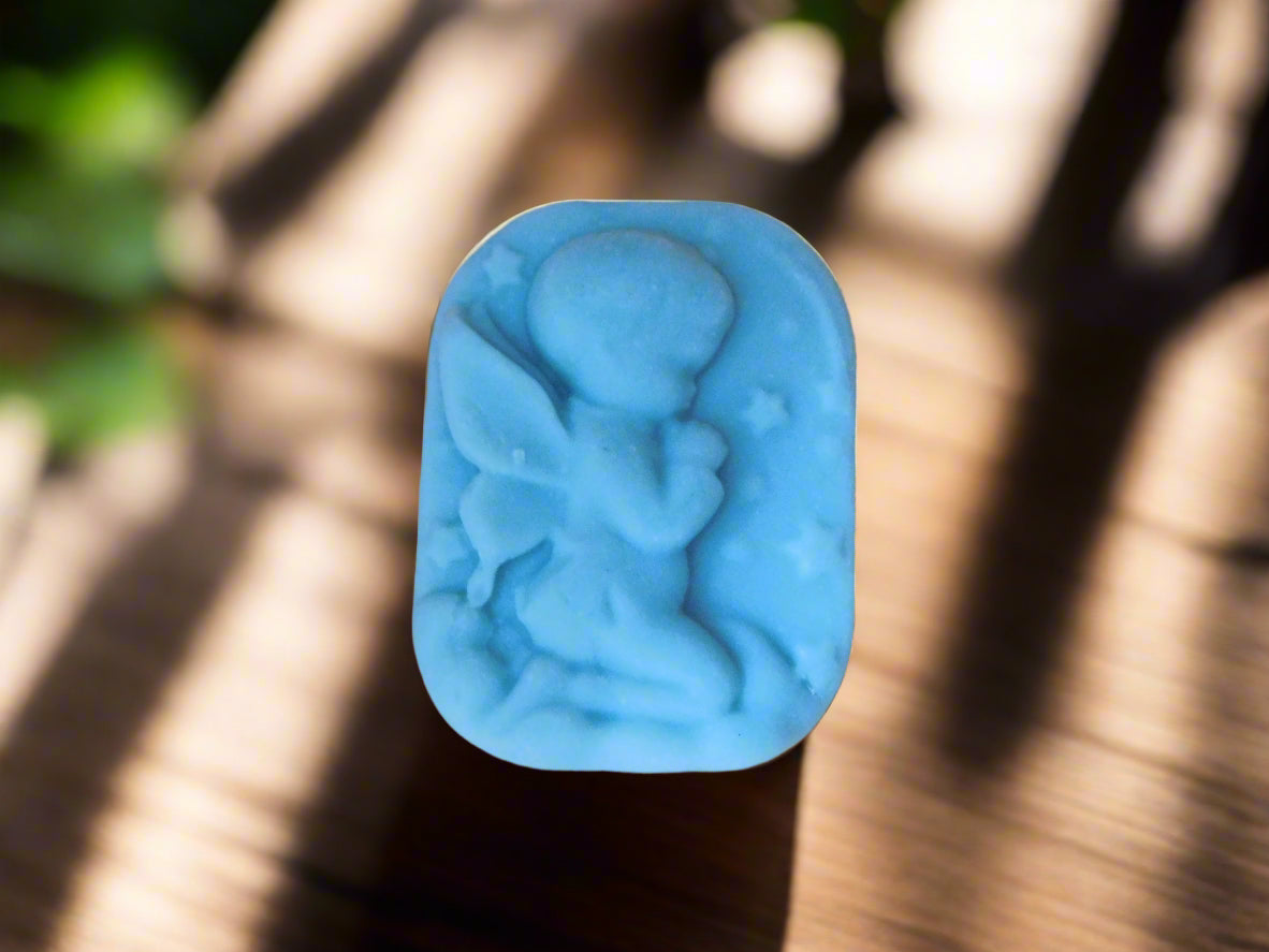 A handmade bar of soap with an embossed boy angel shape design on top, placed on a counter with soft lighting in the background.