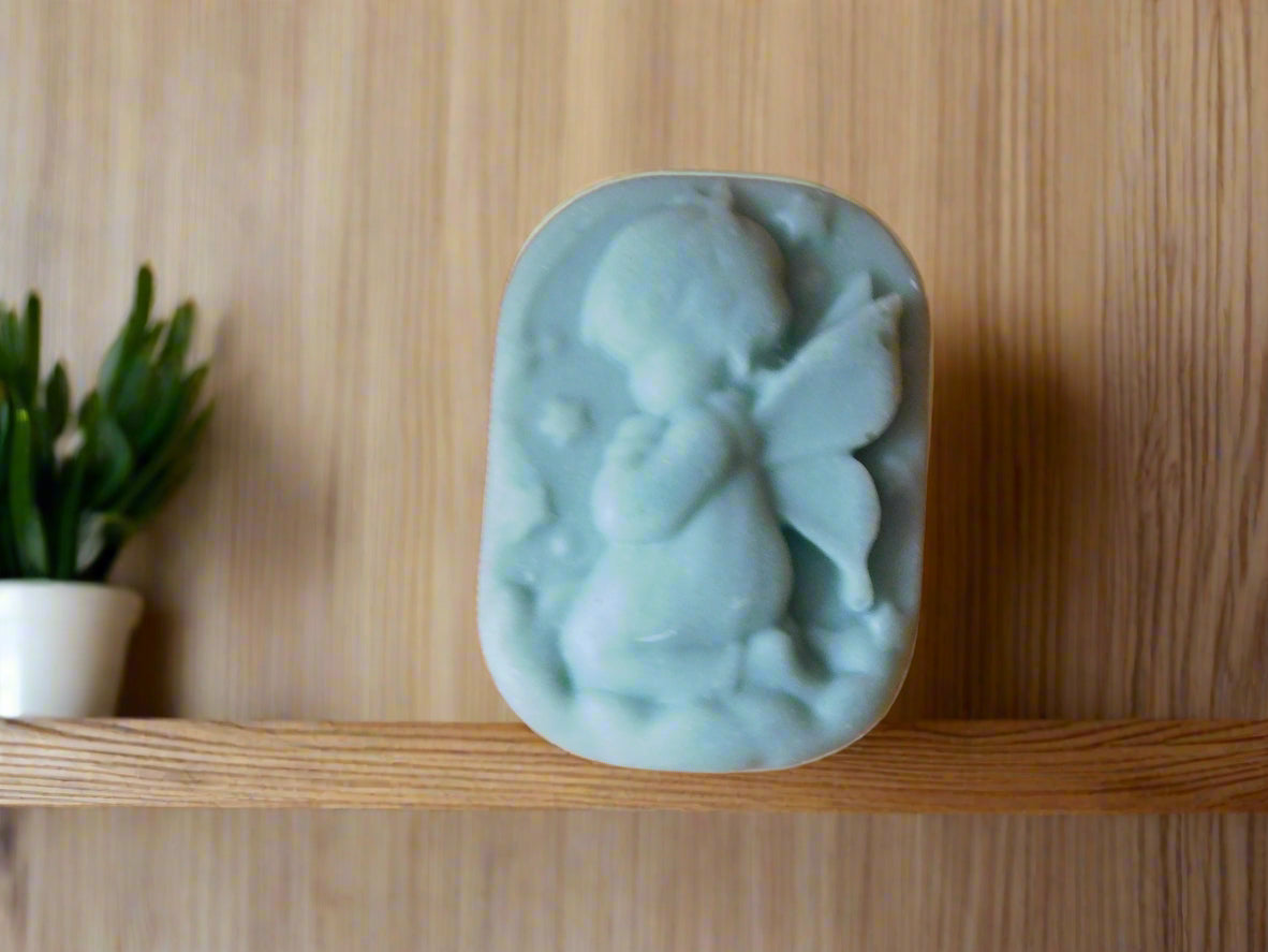 A handmade bar of soap with an embossed girl angel shape design on top, placed on a wooden counter with soft lighting in the background.