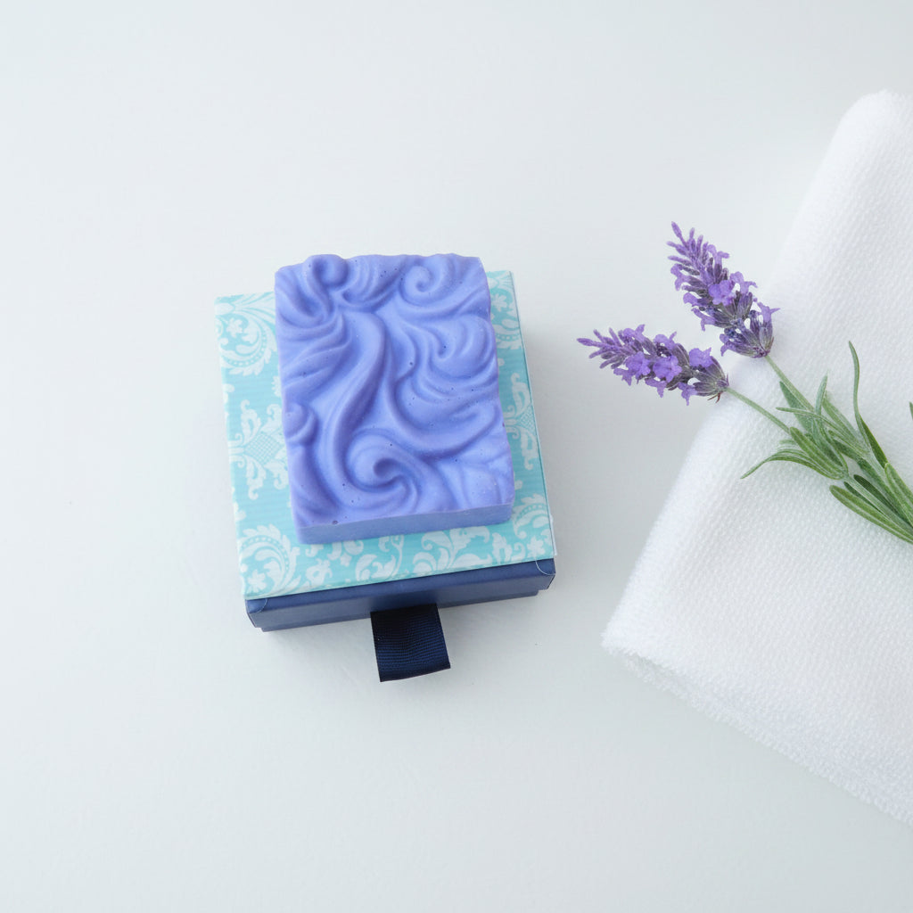 a swirl French lavender soap purple colour in a white background and next to it French lavender flower and a towel