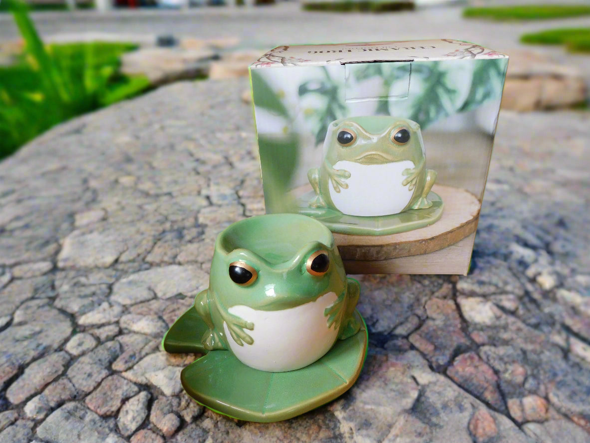 A green ceramic frog-shaped oil burner on a lily pad, displayed on a stone surface.