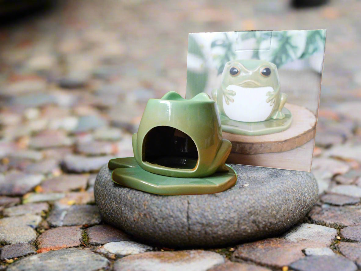 A green ceramic frog-shaped oil burner on a lily pad, displayed on a stone surface view from the back