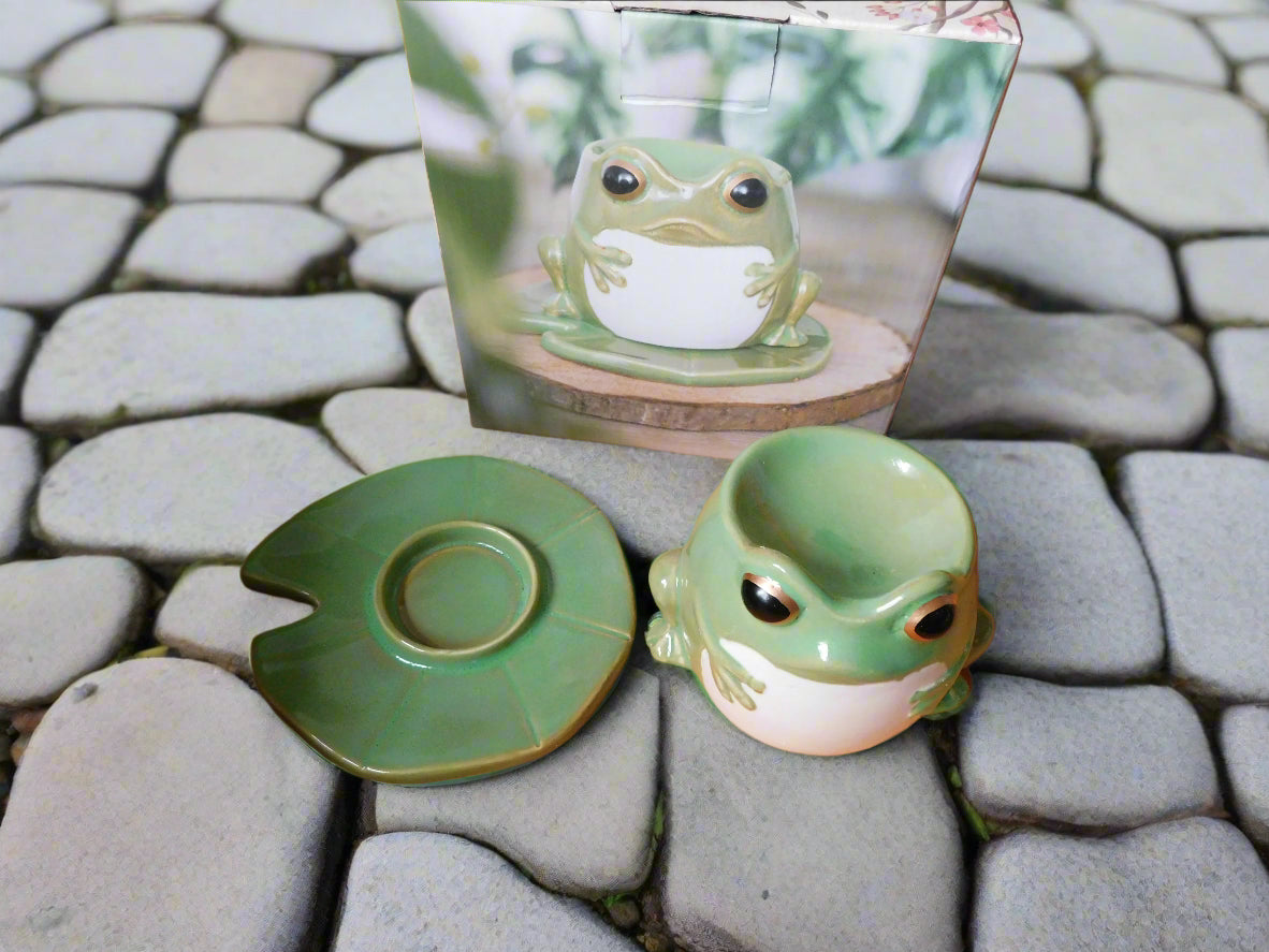 A green ceramic frog-shaped oil burner on a lily pad, displayed on a stone surface view from the top