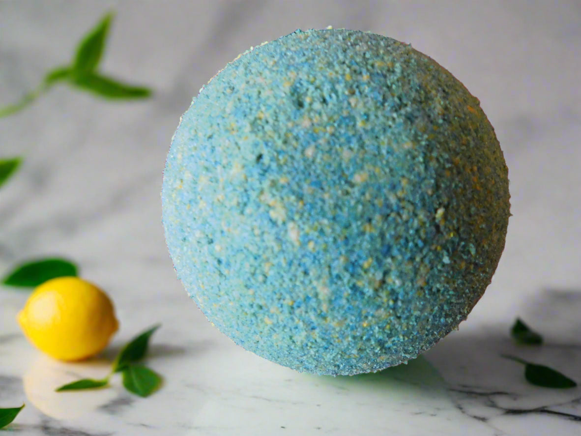 yellow and green round bath bomb with a lemon on the left handside of the bath bomb and leaves of lemon all around it.
