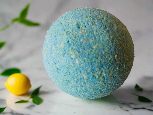 yellow and green round bath bomb with a lemon on the left handside of the bath bomb and leaves of lemon all around it.
