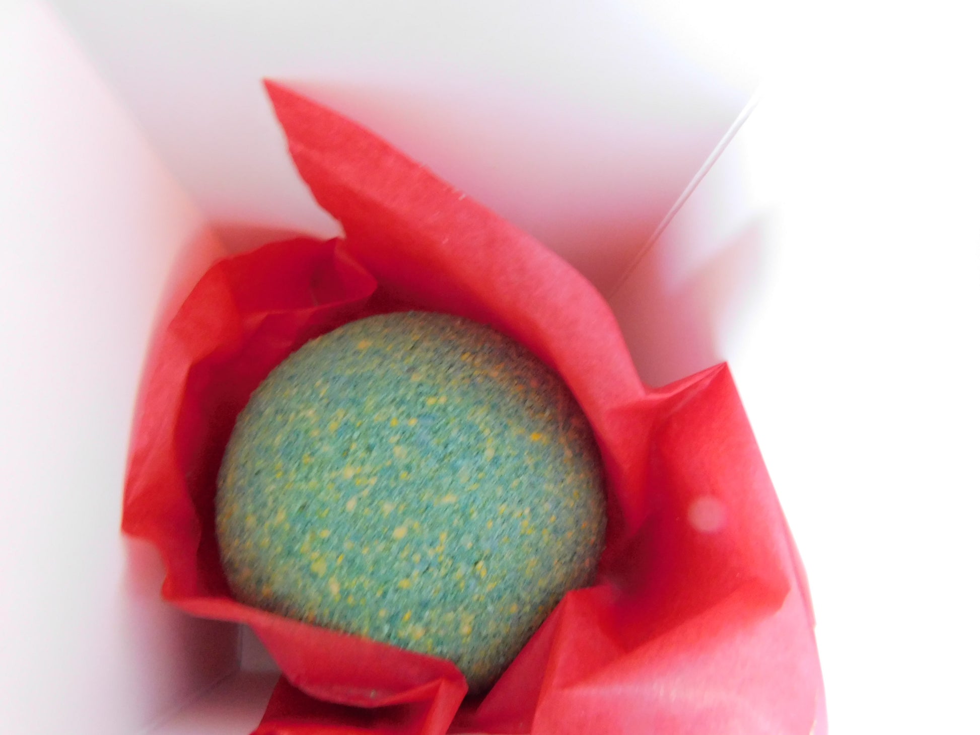 Green and yellow bath bomb in a red paper bag on a white background box