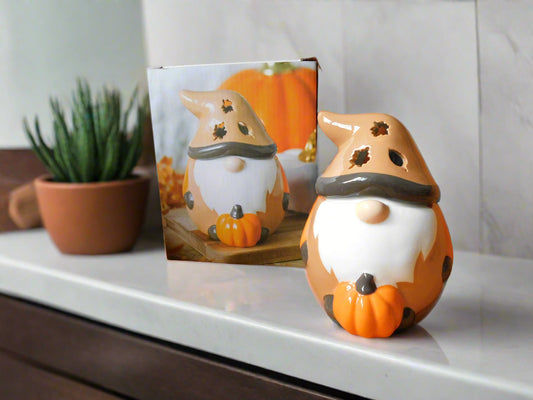Ceramic oil/wax burner with a design resembling a Gonk, in orange and brown colors, placed on a white surface with a plant to its left.