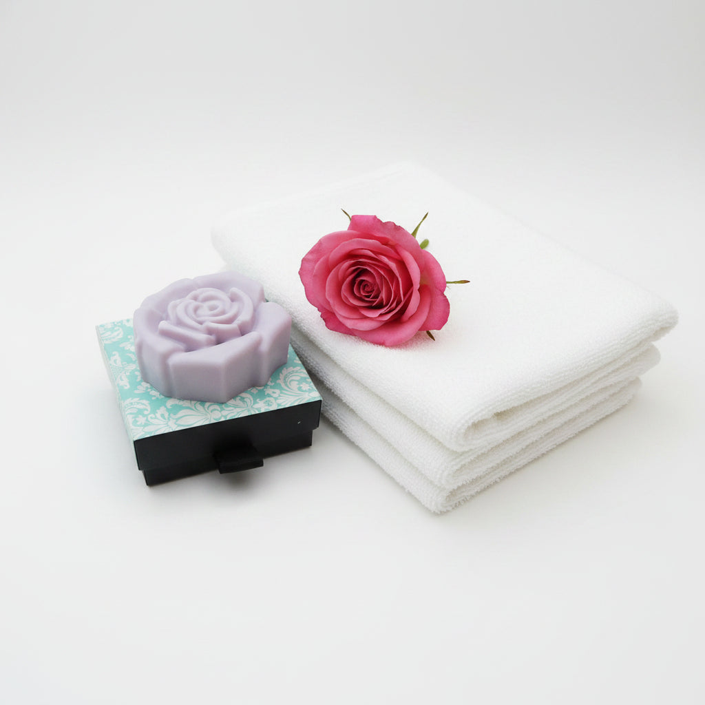 A pink coloured rose-shaped soap bar resting on top of its decorative packaging box, which features a light blue and white damask pattern