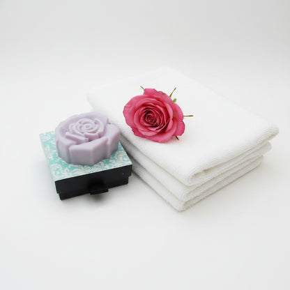 A pink coloured rose-shaped soap bar resting on top of its decorative packaging box, which features a light blue and white damask pattern