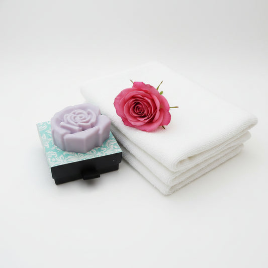 A pink coloured rose-shaped soap bar resting on top of its decorative packaging box, which features a light blue and white damask pattern