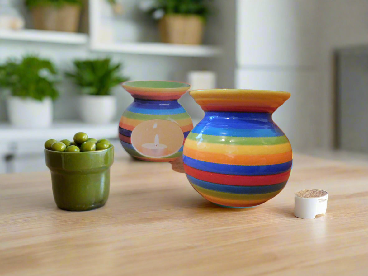 A colorful ceramic oil burner with rainbow stripe patterns on a table, alongside a small green olives container and a white peppercorn box.