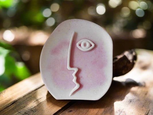 Handmade bar of soap with a floral design and a face silhouette, placed on a wooden surface.