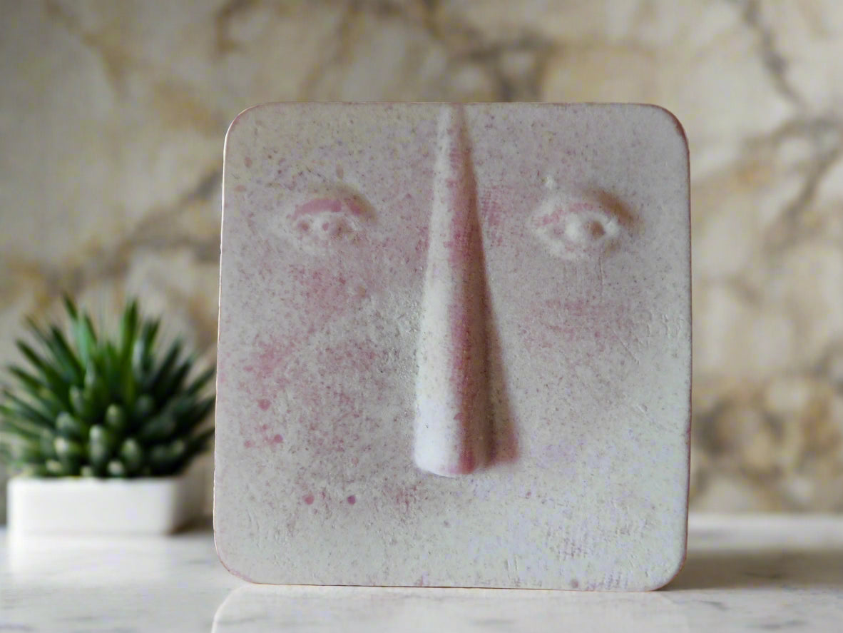 A bar of soap with a geometric rectangular face design on a shelf with plants in the background.