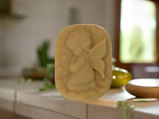 A handmade bar of soap with an embossed girl angel shape design on top, placed on a counter with soft lighting in the background.