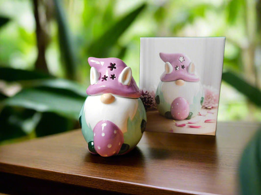 A ceramic oil/wax burner in the shape of a bunny gonk with decorative elements, displayed on a wooden surface with foliage in the background.