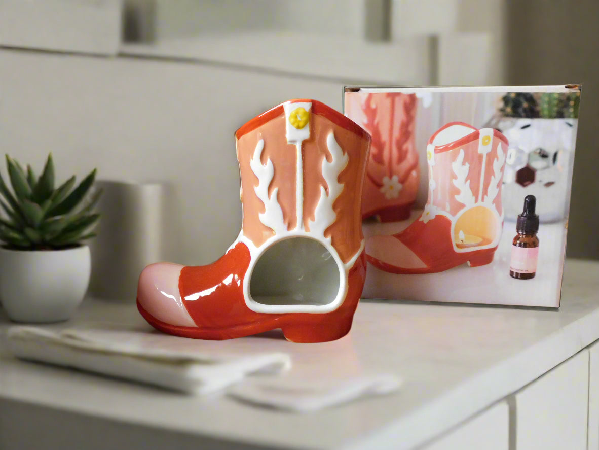A ceramic cowboy boot oil burner and wax warmer in red and white color, displayed alongside its packaging.
