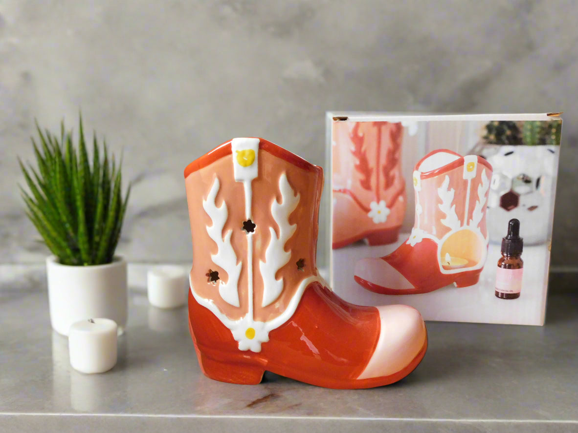 A ceramic cowboy boot oil burner and wax warmer in red and white color, displayed alongside its packaging view from the front