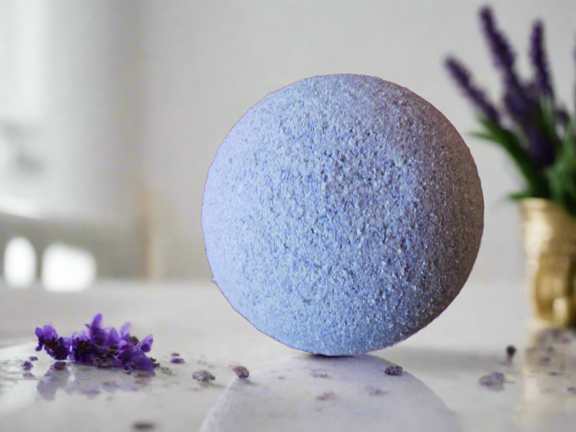 purple lavender bath bomb on the top of the marble counter with some lavender flower next to it.