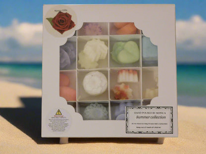 A box of assorted soya wax melts displayed on a sandy beach with a tropical setting in the background.