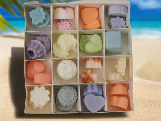 A box of assorted soya wax melts opened box displayed on a sandy beach with a tropical setting in the background.