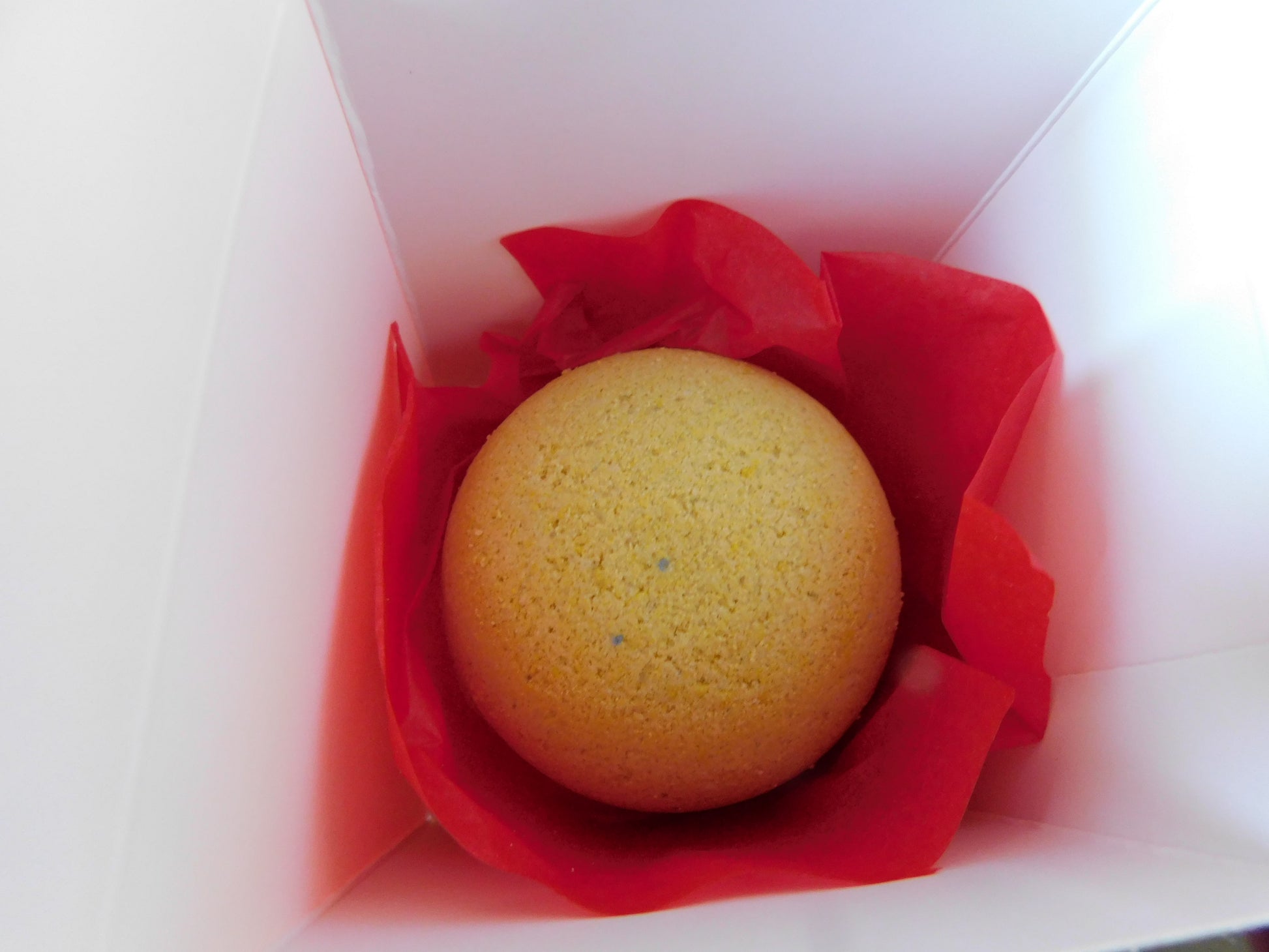 Yellow bath bomb ball in a white box with red tissue paper