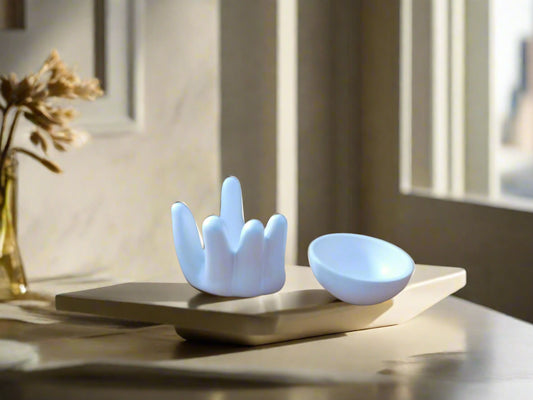 A white ceramic oil burner designed in the shape of a hand, sitting on a table with a bowl in the center. The bowl is on the top of a chopping board